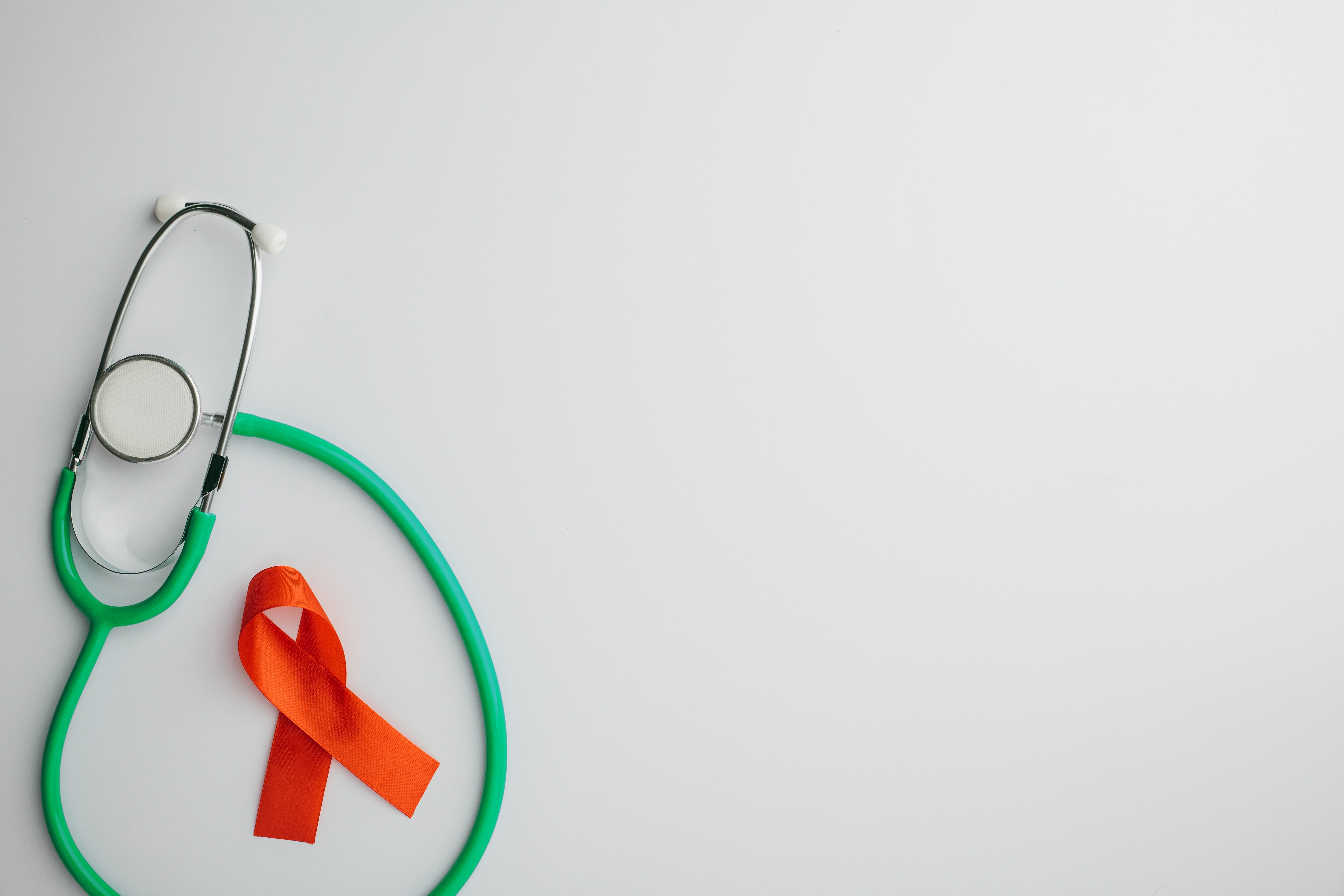 Green medical stethoscope next to an orange awareness ribbon on a white background