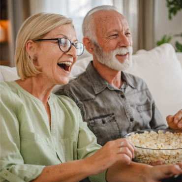 Pareja de adultos mayores disfrutando una película y comiendo palomitas de maíz.